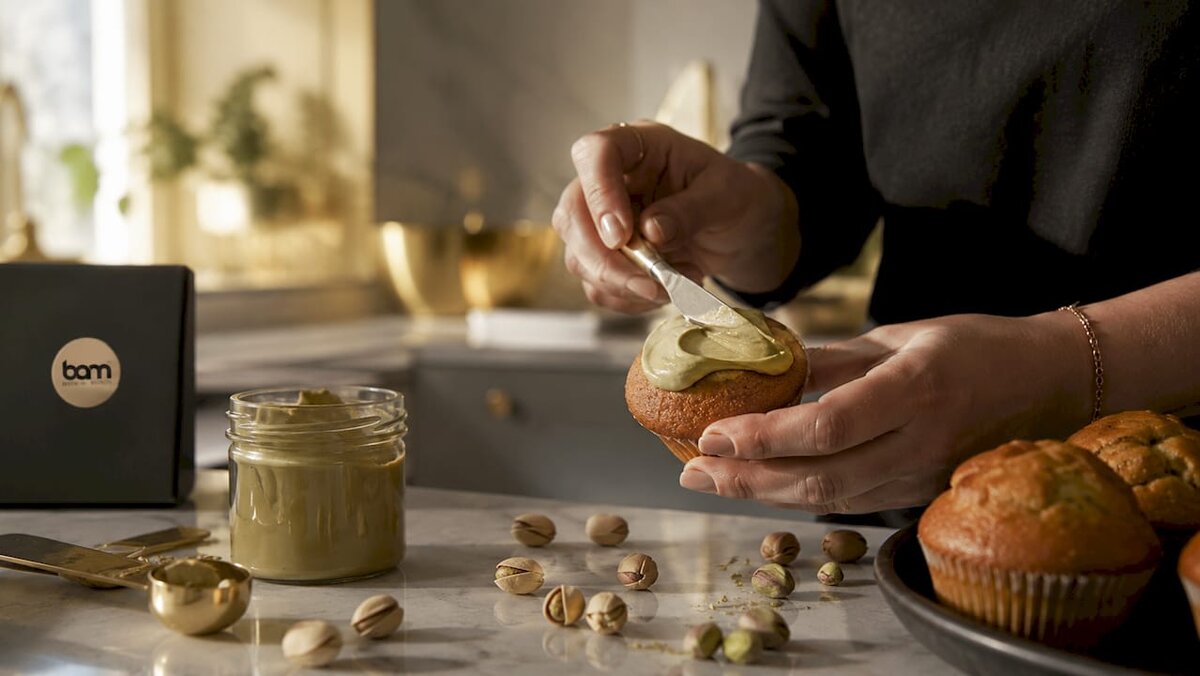 Ruky, ktoré natierajú muffin pistáciovou nátierkou
