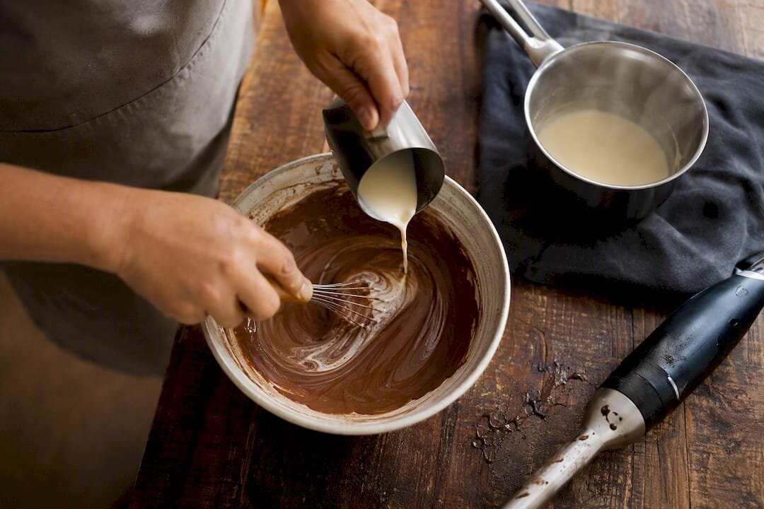 Ruky, ktoré opravujú rozbitú ganache pomocou smotany a metly